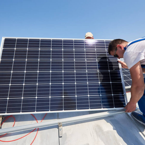 Mężczyźni montują panele słoneczne na dachu w słoneczny dzień.