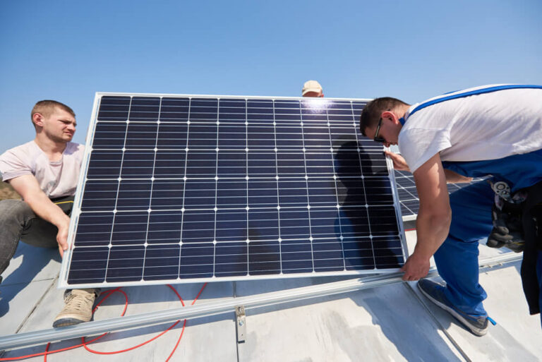 Mężczyźni montują panele słoneczne na dachu w słoneczny dzień.