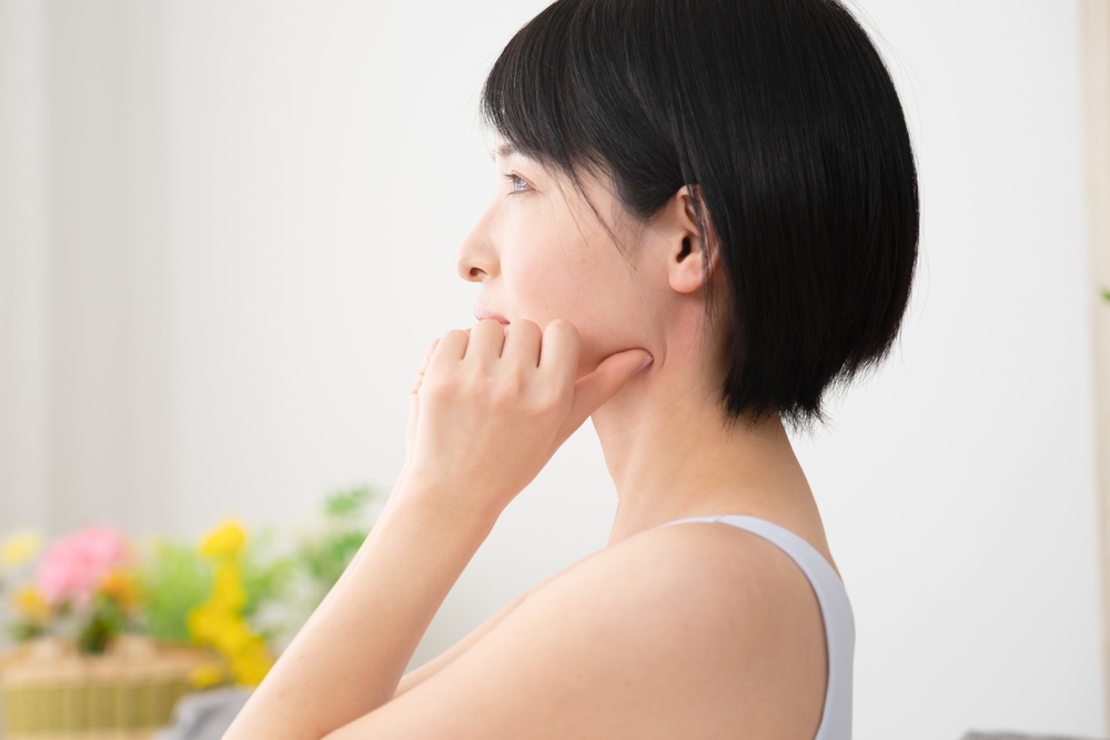 Kobieta z krótkimi włosami myśli, opierając rękę na brodzie, w tle kwiaty.