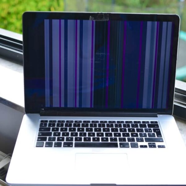 Uszkodzony ekran laptopa z widocznymi pionowymi paskami na czarnym tle, stojący przy oknie.